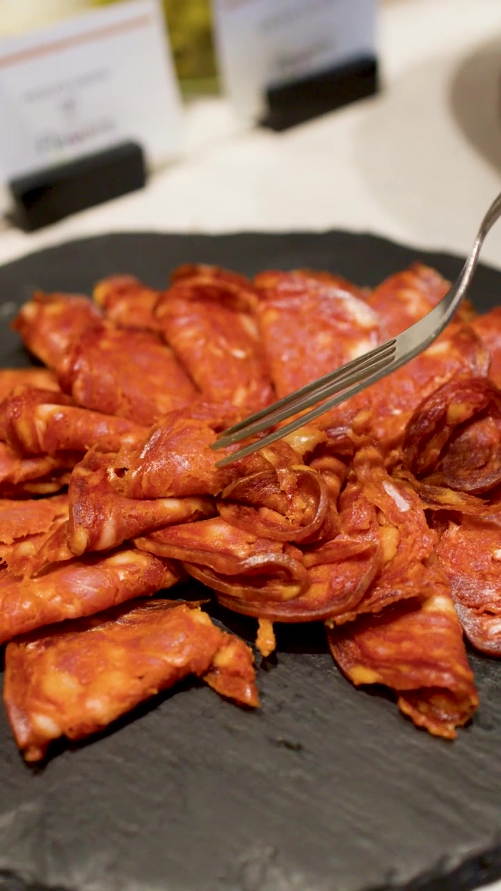 Forchetta che prende chorizo affettato da un piatto di ardesia nero