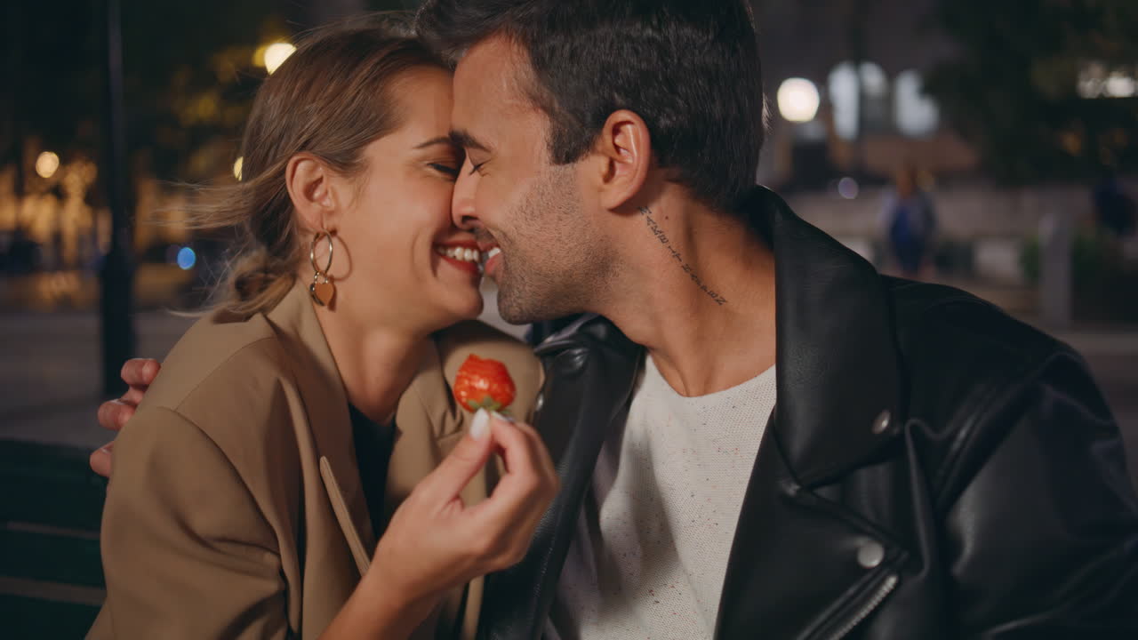 una pareja juguetona disfrutando de una cita besándose de cerca por la noche. una pareja sonriente con fresa