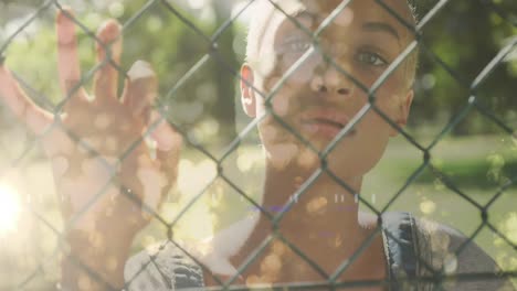 Animation-of-light-trails-over-biracial-woman-standing-behind-fence