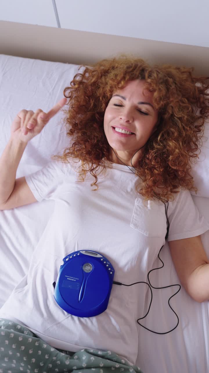 Woman listening to music in bed with CD player and headphones