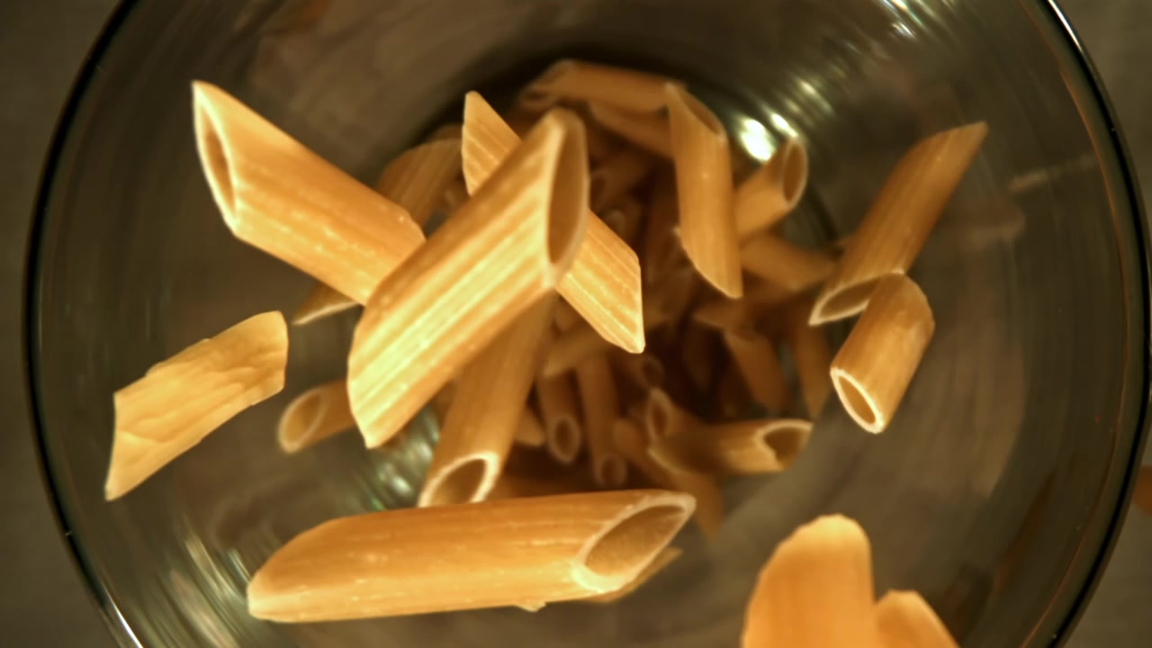 Pasta penne cruda che cade in una ciotola di vetro trasparente