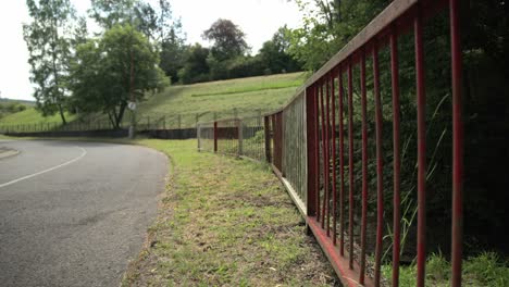 Reverse-dolly-along-metal-rusted-fence-on-countryside-road-above-grassy-shoulder