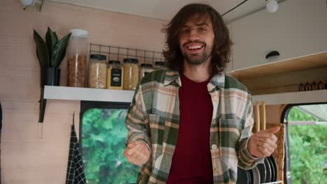 Portrait-of-a-Happy-guy-with-stubble-in-a-Green-checkered-shirt-who-dances-and-has-fun-in-his-motorhome-or-trailer-outside-the-city-during-his-vacation-and-picnic-in-the-summer