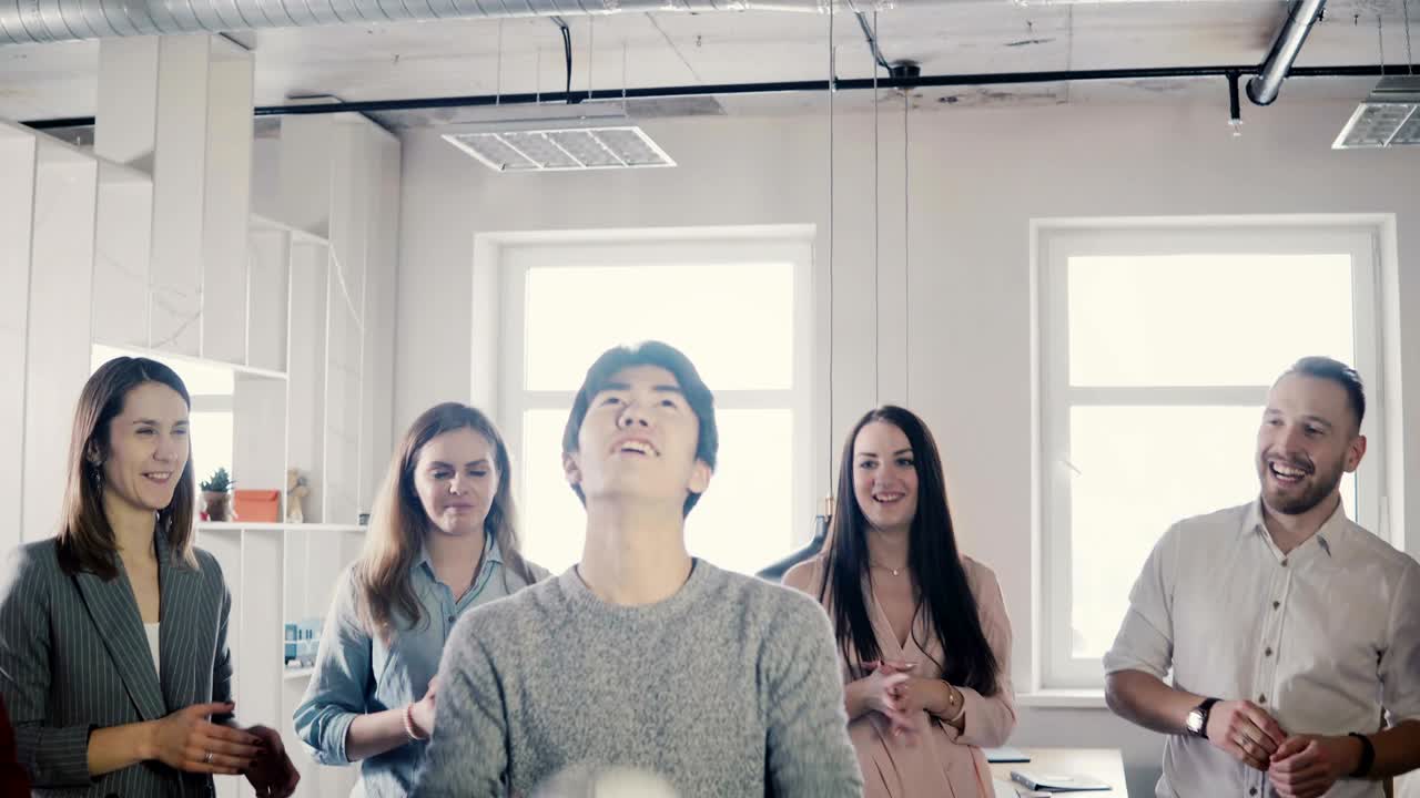 행복한 아시아 남자가 머리에 축구를 조글링하려고합니다. 긍정적 인 혼합 민족 노동자는 사무실에서 재미있는 스포츠 게임을합니다.
