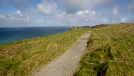 Extraweite-Aufnahme-Des-Sonnendurchfluteten-Küstenwegs-Mit-Blick-Auf-Die-Klippen-Von-Tintagel-Im-Hintergrund,-Vom-Unteren-Penhallischen-Tregatta-Aus