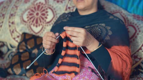 mujer india tradicional sentada en una cama y tejiendo bufanda en color rojo y negro