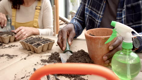 midsection of diverse mature couple planting seedlings in pots on table in garden, slow motion