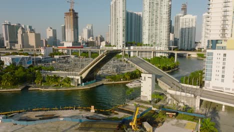 boat driving on river in city, passing under double leaf bascule road bridge. scene lit by setting sun. miami, usa