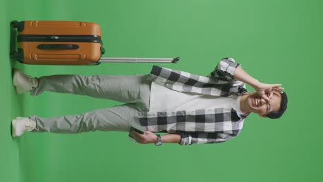 full body of asian male traveler with luggage and passport smiling and showing ok hand sign over eye while standing in the green screen background studio