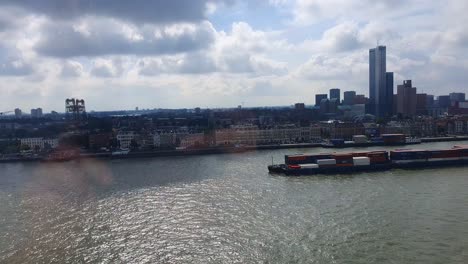 view through window of container barge going past on nieuwe maas with rotterdam skyline in background