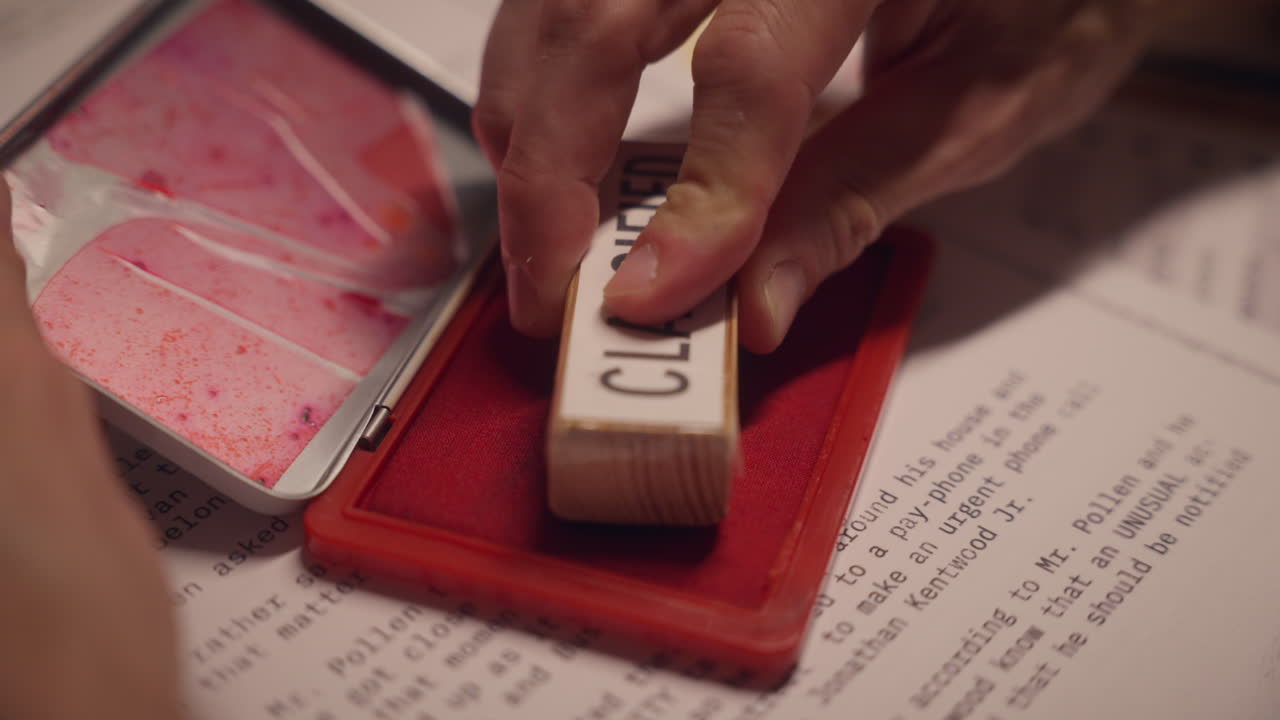 Close up on red ink pad as hand press stamp to mark document as classified. Government official or agent labeling papers for censorship and archive. Sensitive information to be kept secret and hidden