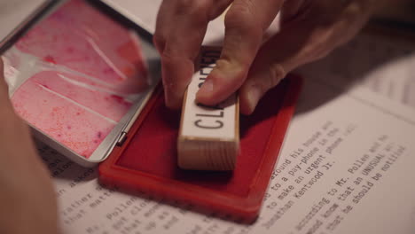 close up on red ink pad as hand press stamp to mark document as classified. government official or agent labeling papers for censorship and archive. sensitive information to be kept secret and hidden