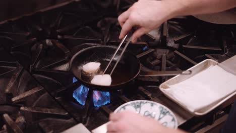 man puts the chicken with a silver skewer in a frying pan with hot oil in a restaurant kitchen