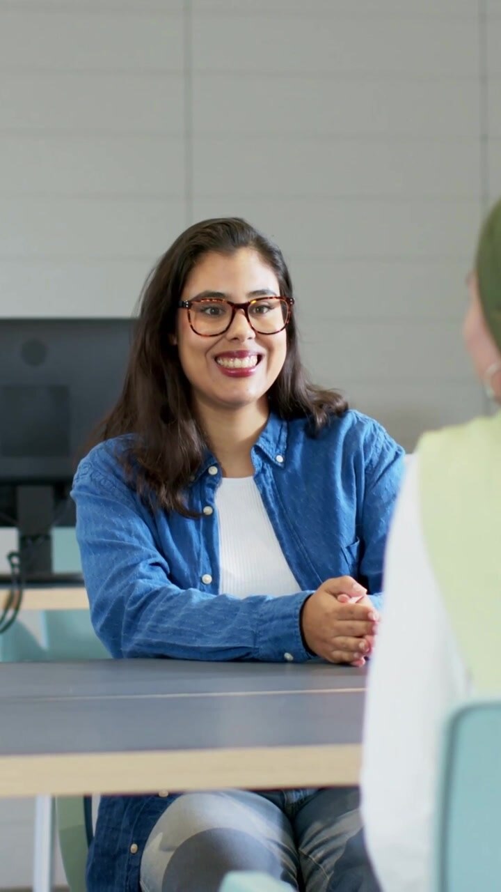 Vertical video: Talking woman in blue shirt gesturing offering handshake in meeting room with specs