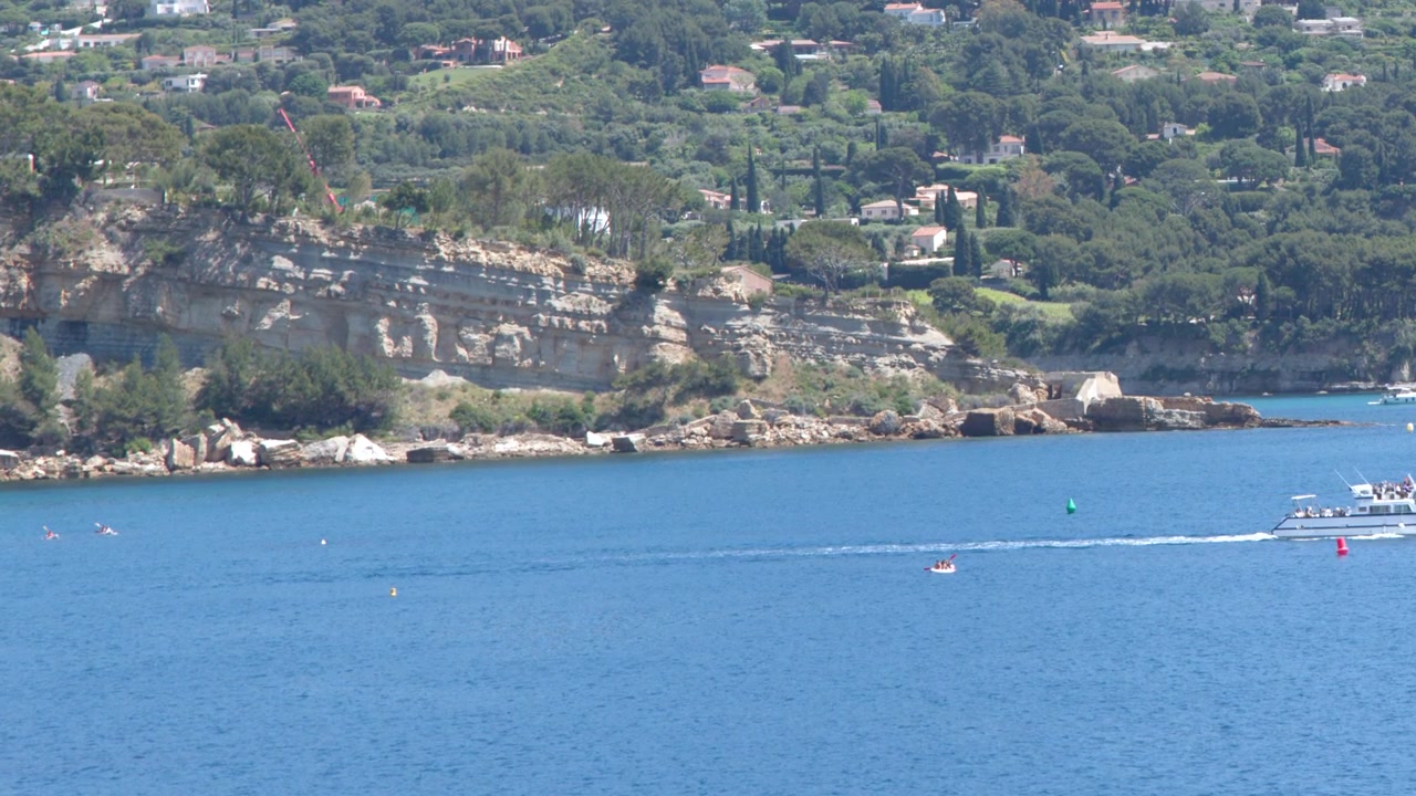 Inquadratura ampia di una barca bianca che naviga su acqua blu vicino a scogliere rocciose e colline.