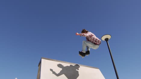 hombre caucásico montando y saltando en patineta en un día soleado