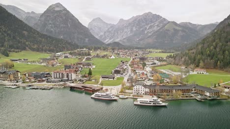 a captivating drone shot at achensee pertisau, flying away with passenger boats below and majestic mountains in the background. a stunning alpine lake scene showcasing natural beauty.