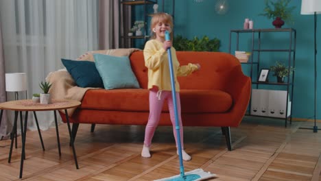 child girl kid washes floors with a mop in domestic living room dancing, singing in positive mood