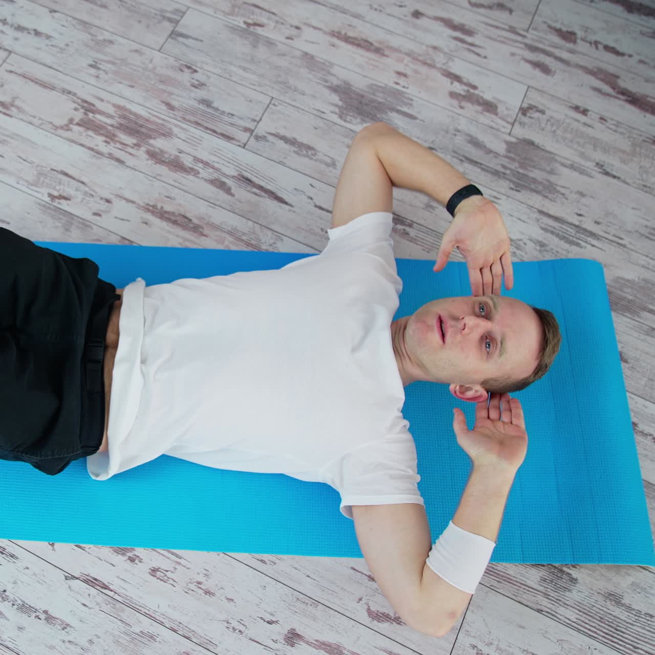 Man training at home. Keeping fit. Young man in white t-shirt and black pants doing workout on a mat. Sport and health. Top view