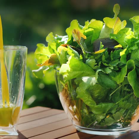 in a glass a green cocktail of lettuce is poured next to a bowl of greens