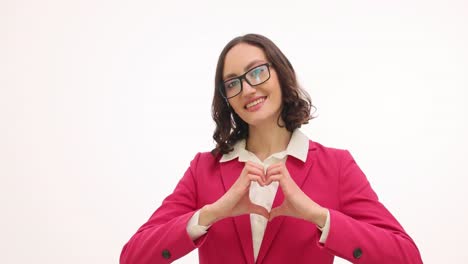 Smiling woman in pink blazer making heart gesture on white background
