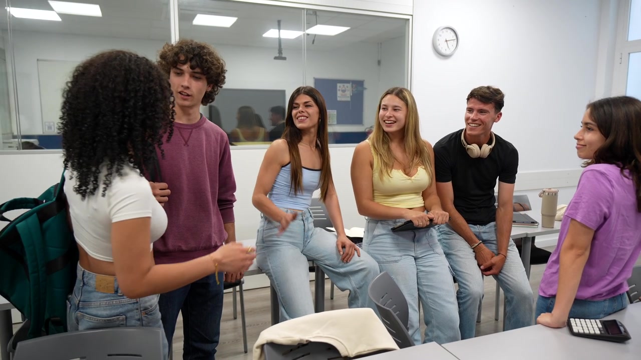 Grupo feliz de estudiantes diversos hablando y saludándose en un aula.