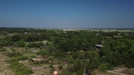 Beautiful-aerial-view-of-white-painted-steel-lighthouse-with-red-top-located-in-Pape,-Latvia-at-Baltic-sea-coastline-in-sunny-summer-day,-wide-angle-drone-shot-moving-backwards