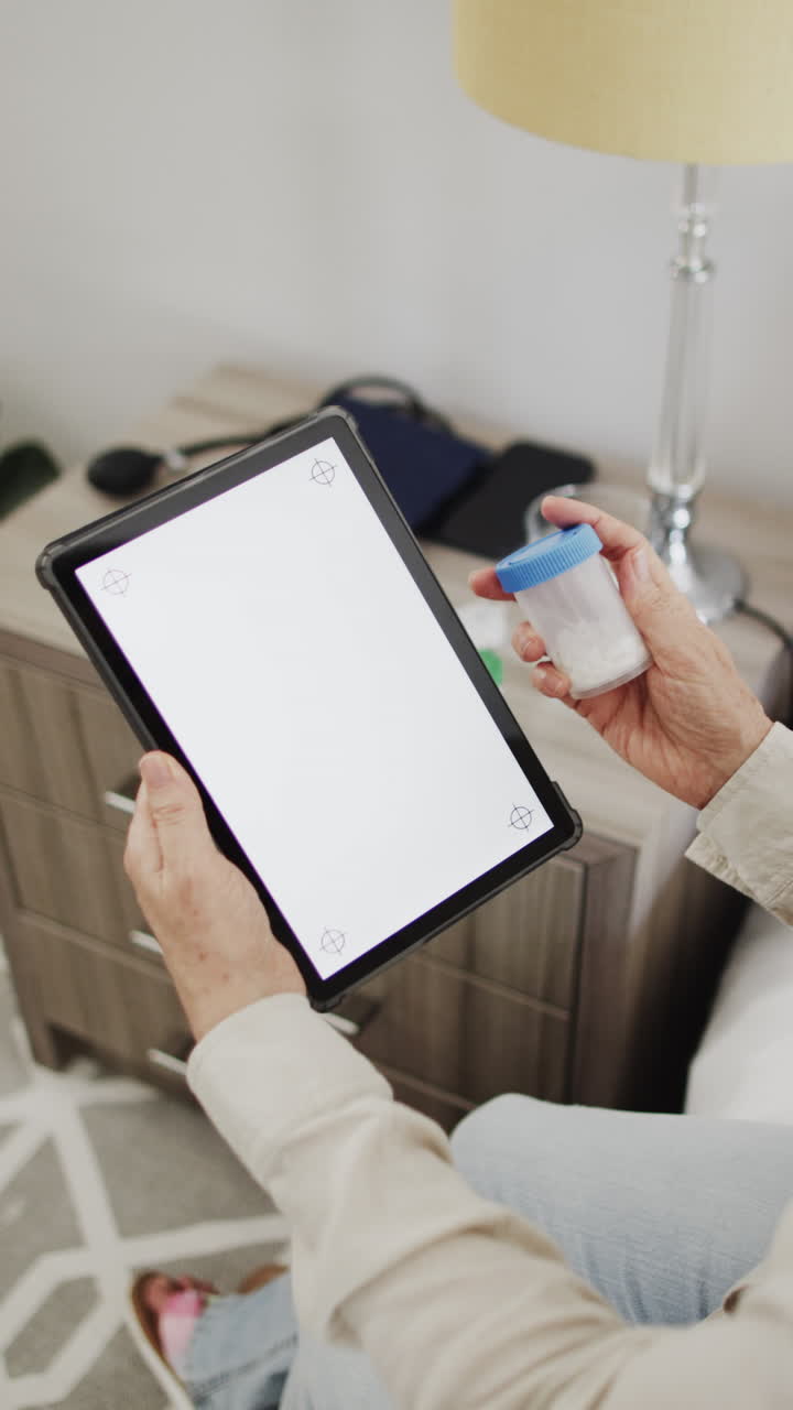 Vertical video of senior caucasian woman holding tablet with copy space and medication, slow motion