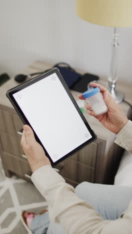 vertical video of senior caucasian woman holding tablet with copy space and medication, slow motion