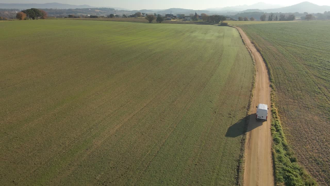 Aerial video of a newly seeded field with a dirt road in the middle and mountains in the background green Llagostera Gerona cultivated field Chasing a white van