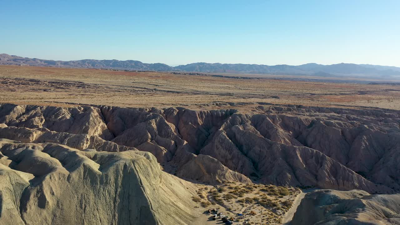 paisaje aéreo drone slider shot volando sobre colinas arroyo tapiado cuevas de barro hacia las montañas en un día cálido, seco y soleado con cielos azules