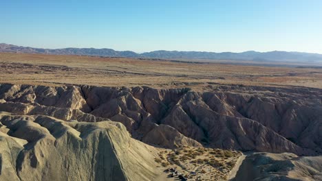 Drohnen-Schieberegler-Aus-Der-Luft,-Der-An-Heißen,-Trockenen,-Sonnigen-Tagen-Mit-Blauem-Himmel-über-Hügel-Arroyo-Tapiado-Schlammhöhlen-In-Richtung-Berge-Fliegt