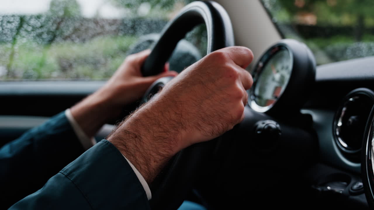 Close up of a man's hands on a steering wheel, driving a car on the road in the rain