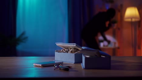 in the foreground the jewels are lying on the table and behind the robber in a black balaclava with a flashlight