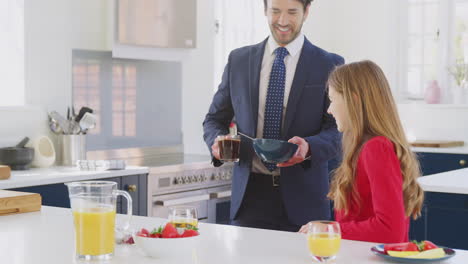 father wearing suit having breakfast with teenage daughter in school uniform at home in kitchen