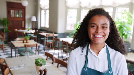 Portrait-Of-Waitress-Standing-In-Empty-Restaurant-Before-Start-Of-Service