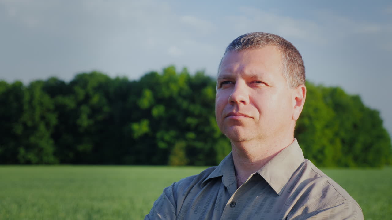 A Man Is Standing In A Field Looking Into The Distance Portrait Of A Farmer Against A Green Wheat Fi