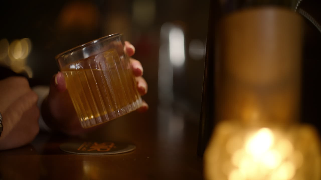 Alone at the bar, a person gently holds a glass of drink, gazing at it thoughtfully