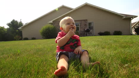 a baby sits in the grass sucking his finger and smiling