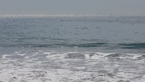 wide view of surfer paddling above clear aqua water and small waves