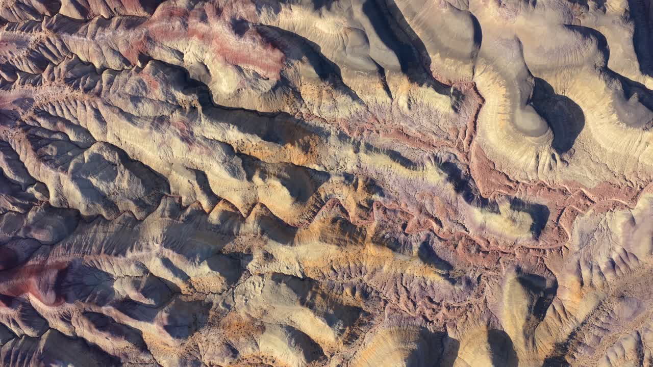 This abstract aerial perspective highlights the vibrant striated textures of the Painted Desert badlands. The unique geological patterns create an alien environment