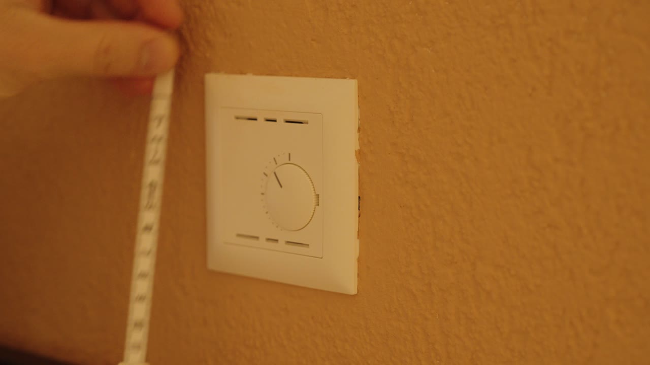 Close-up of hands measuring the distance around a wall thermostat using a tape measure. Concept for home renovation, precision, or energy control