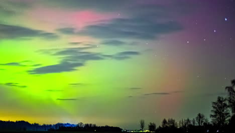 las luces verdes de la aurora bailan a través del cielo rosado de la noche sobre el bosque mientras pasan las nubes.