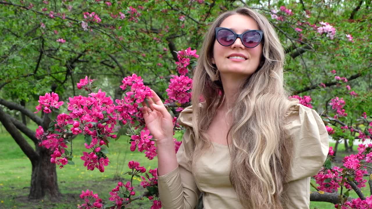 Donna bruna con un vestito marrone vicino a un albero in fiore in un parco