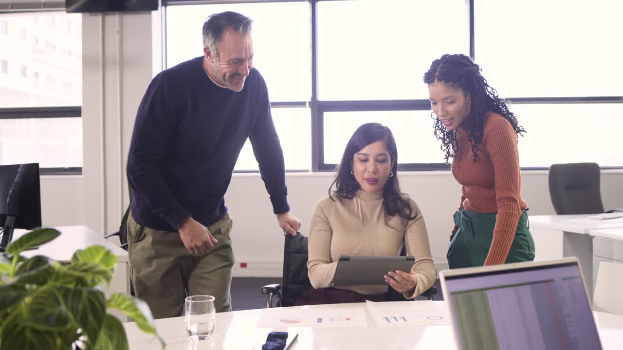 Compañeros de trabajo diversos reunidos alrededor de una tableta en la oficina, un colega masculino señalando un gráfico y guiando a una mujer que la está usando.