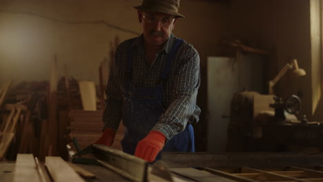 Älterer-Mann-Benutzt-Sägemaschine-Im-Innenbereich.-Ernsthafter-Mann,-Der-Im-Studio-Mit-Holz-Arbeitet