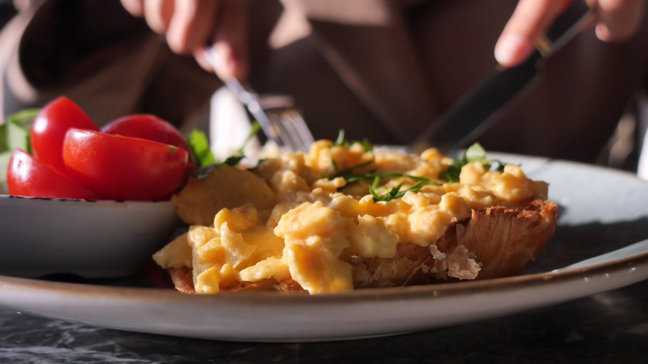 Person Eating Scrambled Eggs on Toast with Cherry Tomatoes
