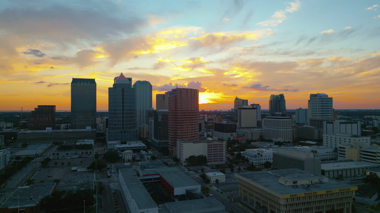 Tampa city skyline as the sun is setting behind the tall buildings with glowing in the light. Aerial building tracking shot