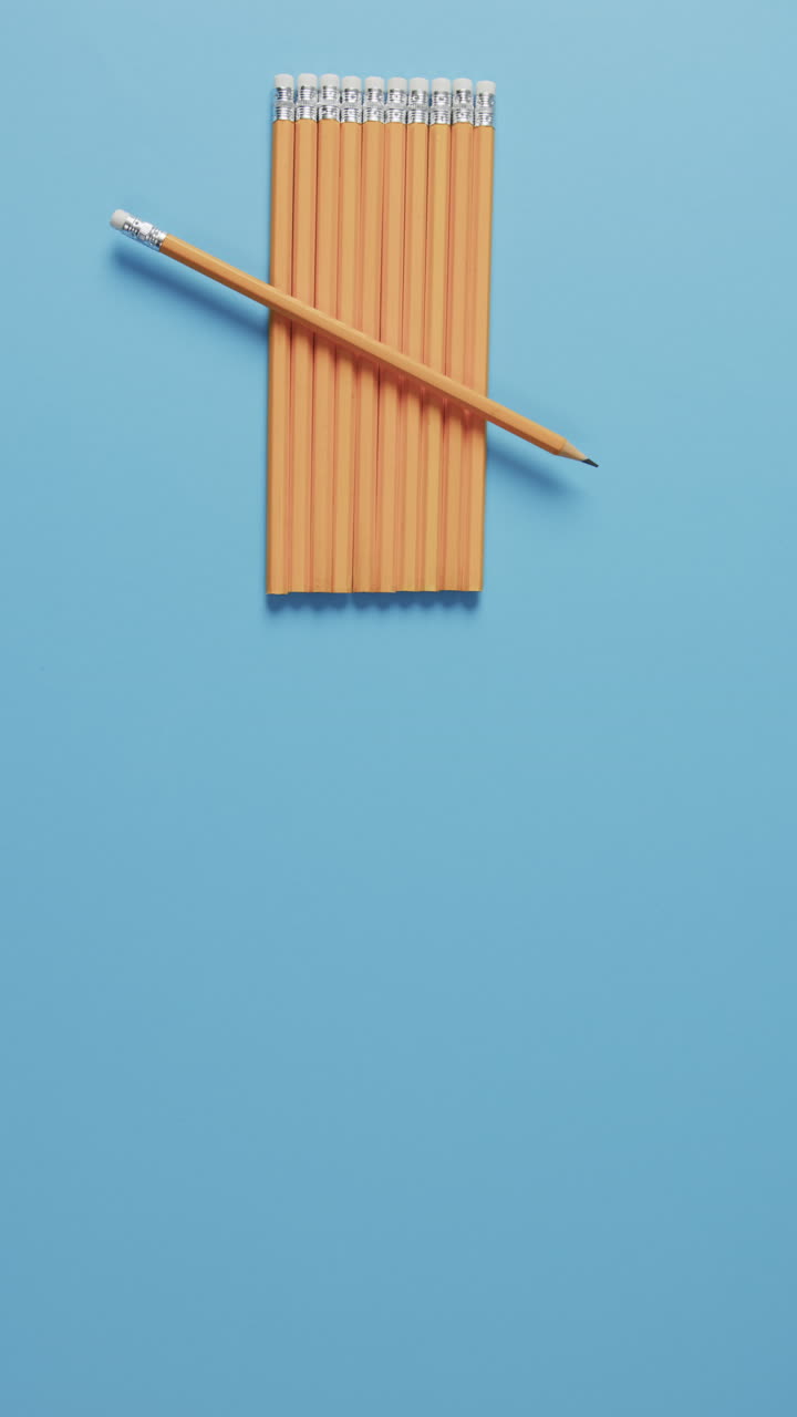 Vertical video of overhead view of pencils with copy space on blue background, in slow motion