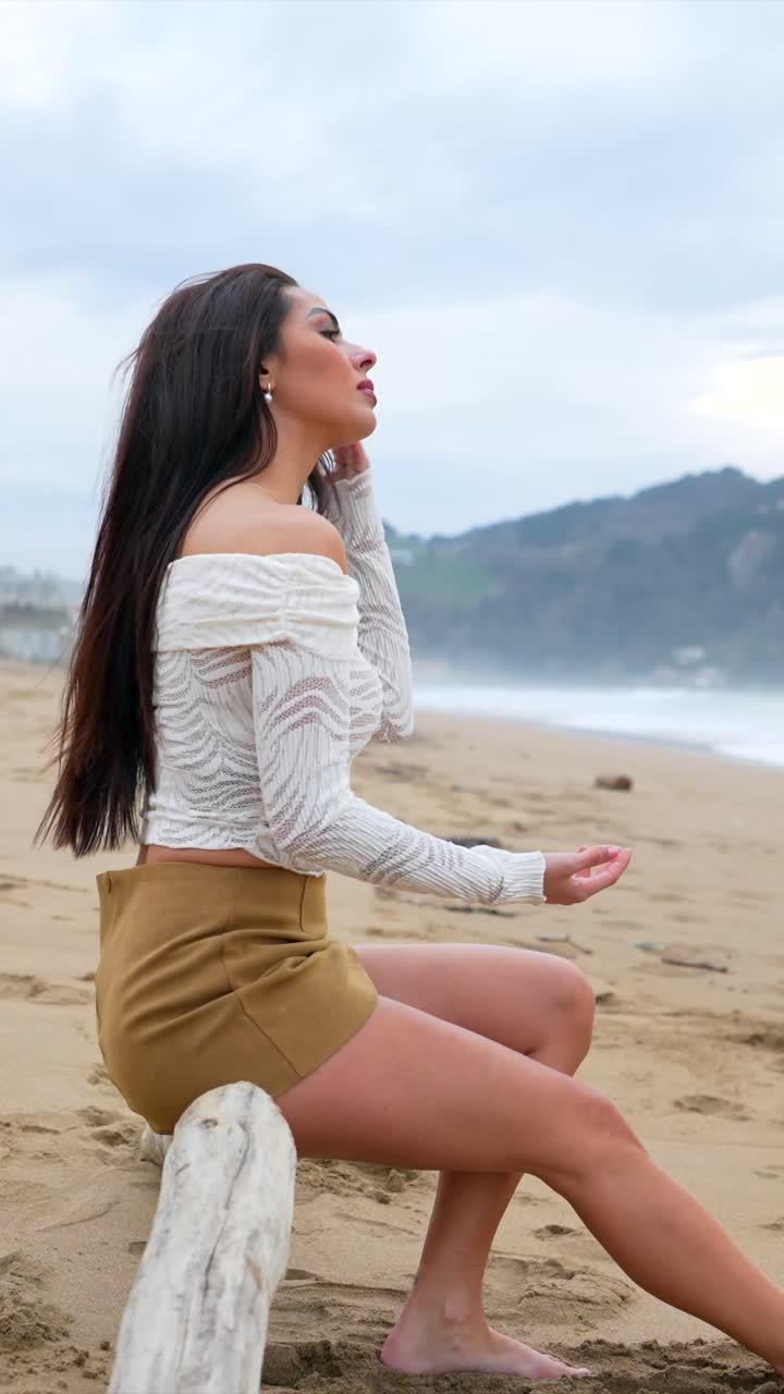 Woman sitting on driftwood at the beach